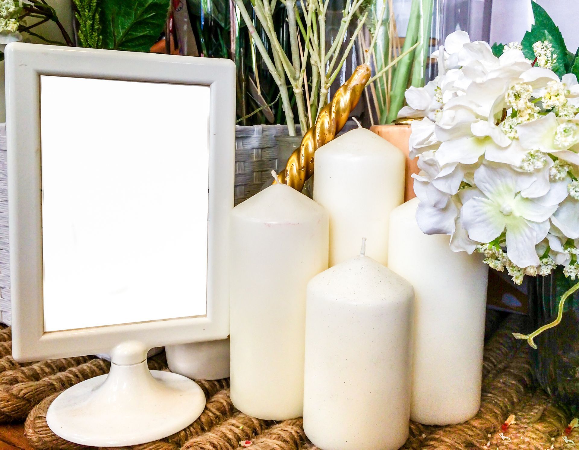 White frame, candles, and flowers arranged on a woven mat.