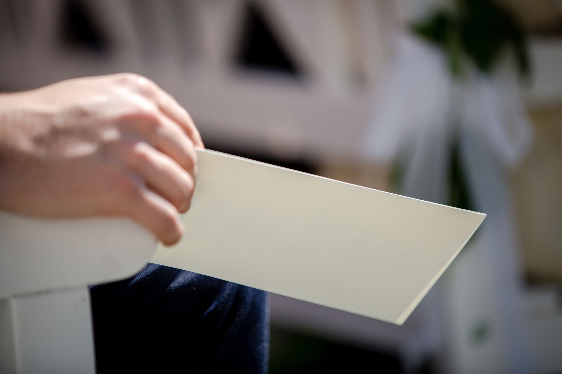 Person's hand holding a cream-colored rectangular card; blurred background.