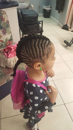 A little girl with braids and a pink backpack is standing in a room.