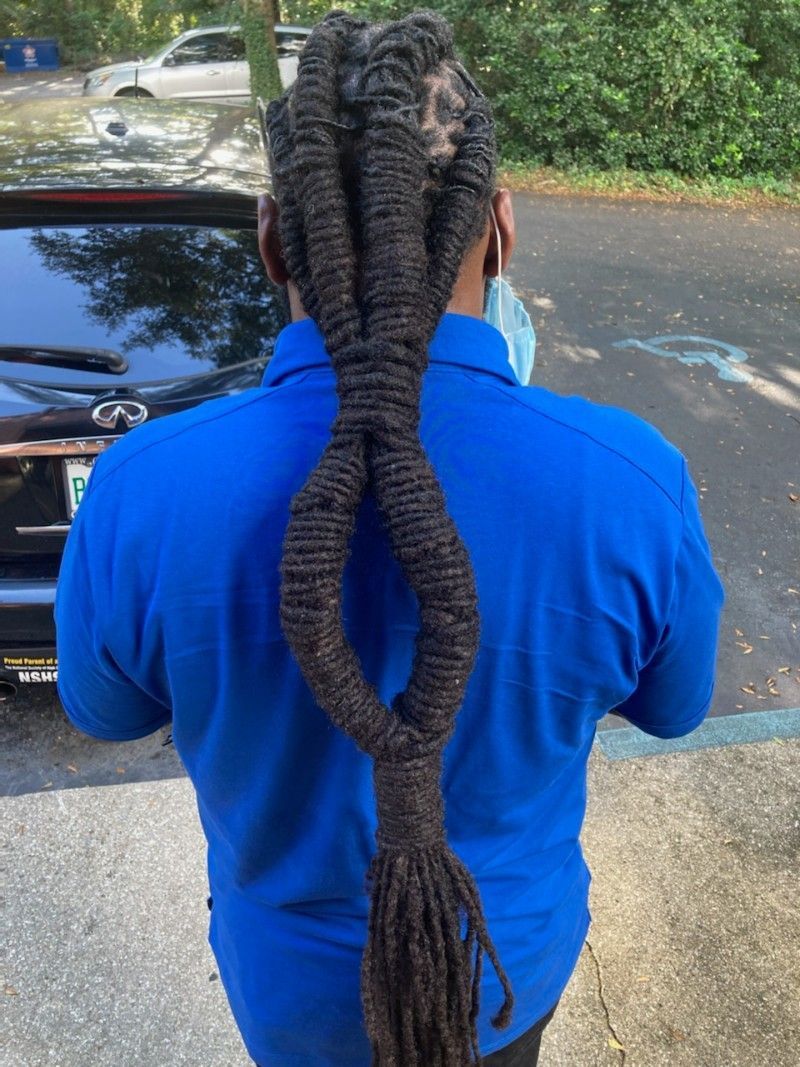 A man with dreadlocks is wearing a blue shirt and standing in front of a car.