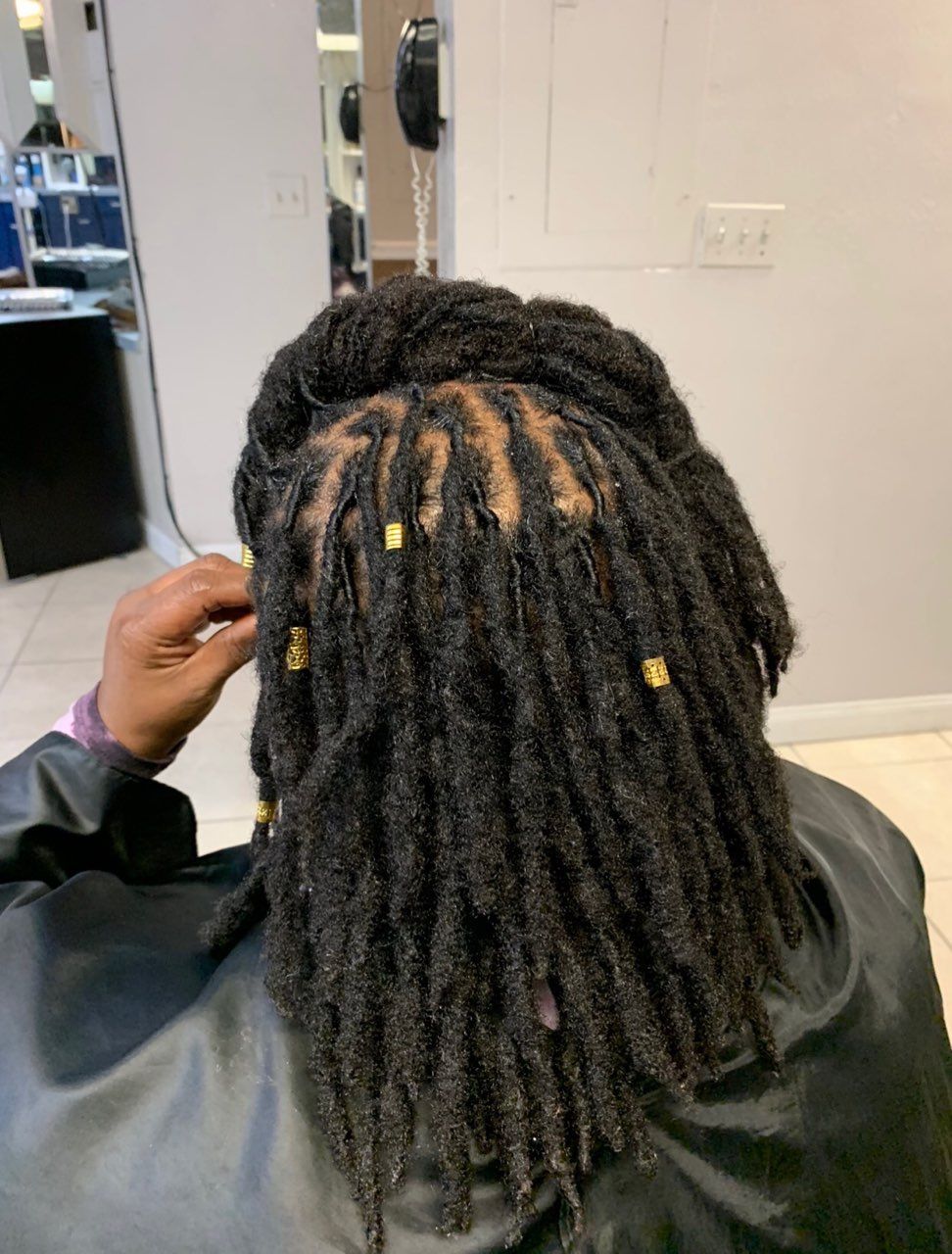 A person with dreadlocks is getting their hair done in a salon.