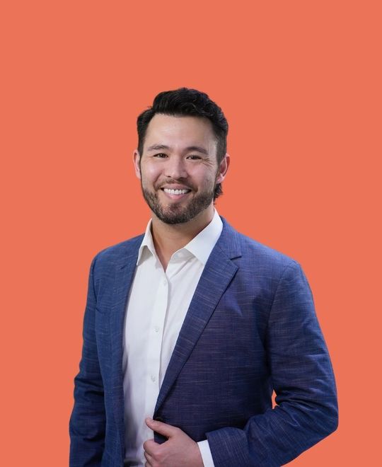 Smiling man, wearing a blue blazer and white shirt, poses against an orange background.