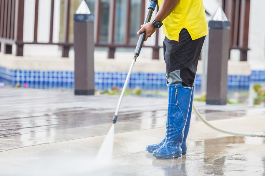 Worker in yellow shirt power-washing a wet pavement with blue boots