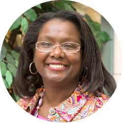 A woman wearing glasses and a paisley jacket smiles for the camera