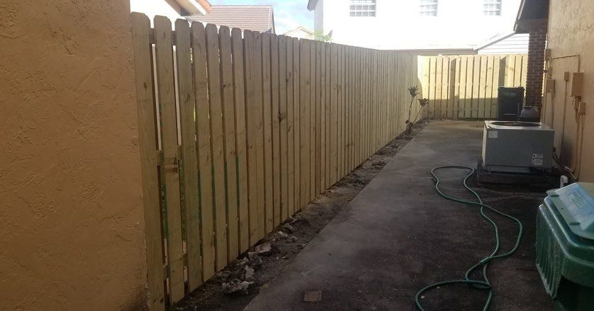 A wooden fence is sitting next to a wall in a backyard.