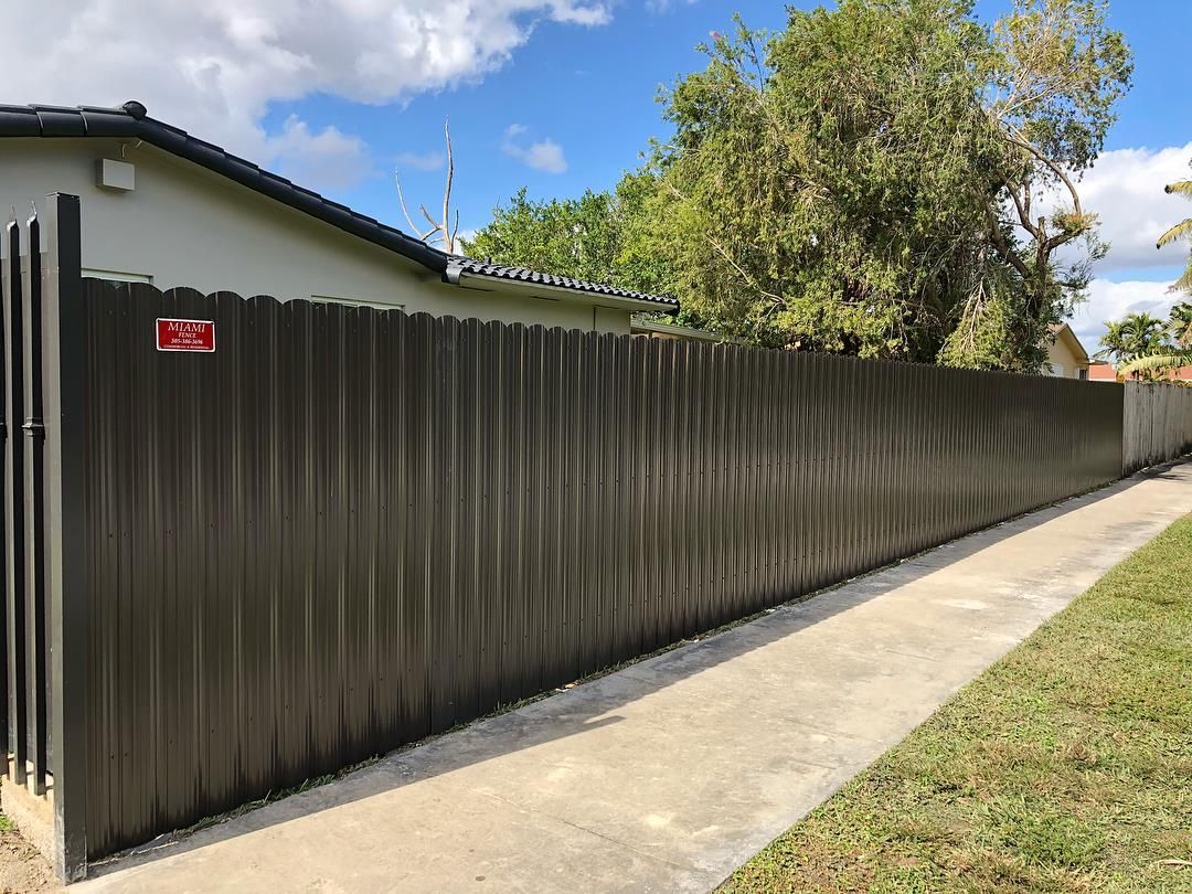A long fence along a sidewalk next to a house.