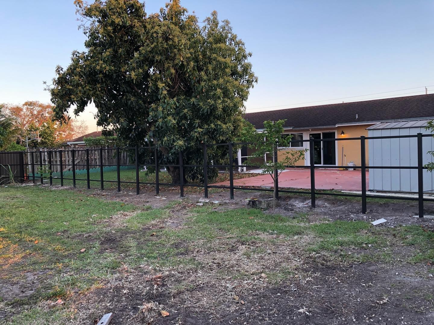 A fence is surrounding a yard with a house in the background.