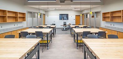 A large classroom with lots of wooden tables and chairs.
