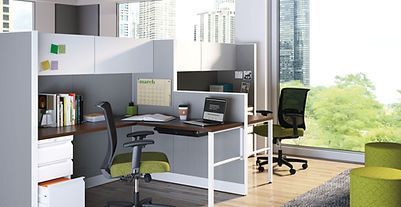 A cubicle with a desk and chairs in a room with a window.