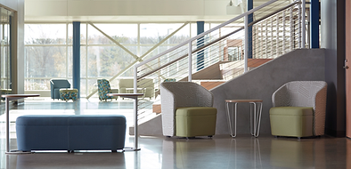 A lobby with chairs , tables and stairs in a building.