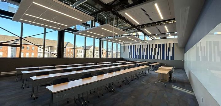 A large classroom with rows of tables and chairs and a podium.