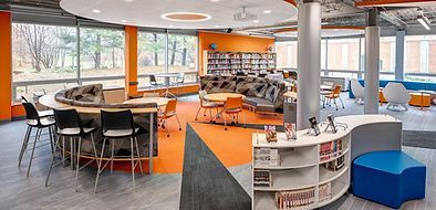 A large room with tables , chairs , and shelves in a library.