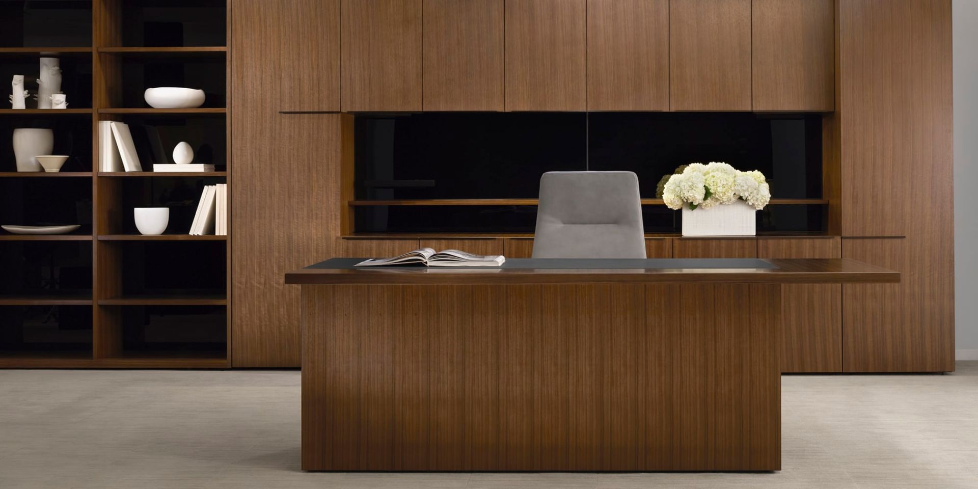 A wooden desk with a chair in a room with shelves.
