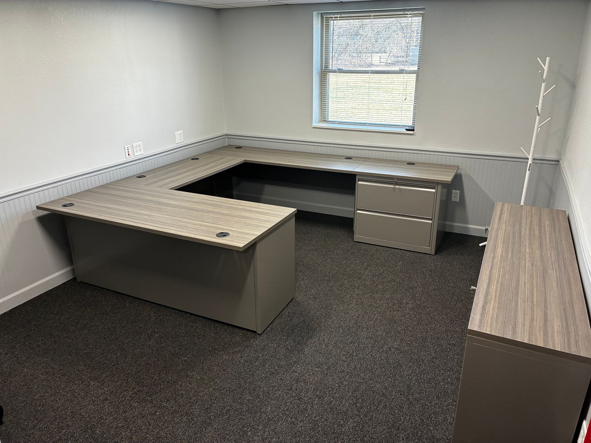 A small office with a desk , drawers , and a window.
