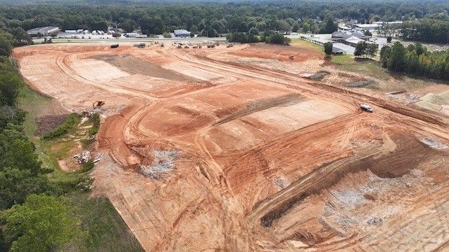 An aerial view of a construction site with a lot of dirt and trees in the background.