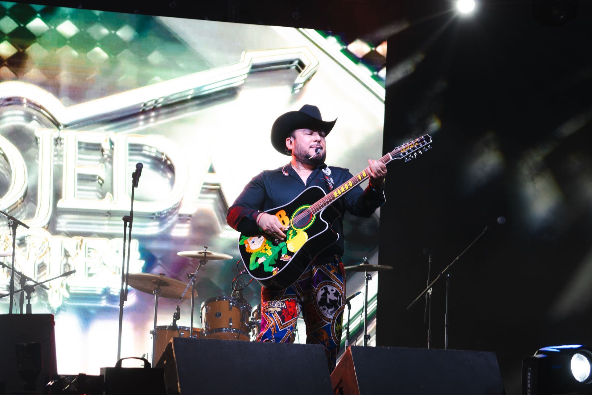 A man in a cowboy hat is playing a guitar on a stage.