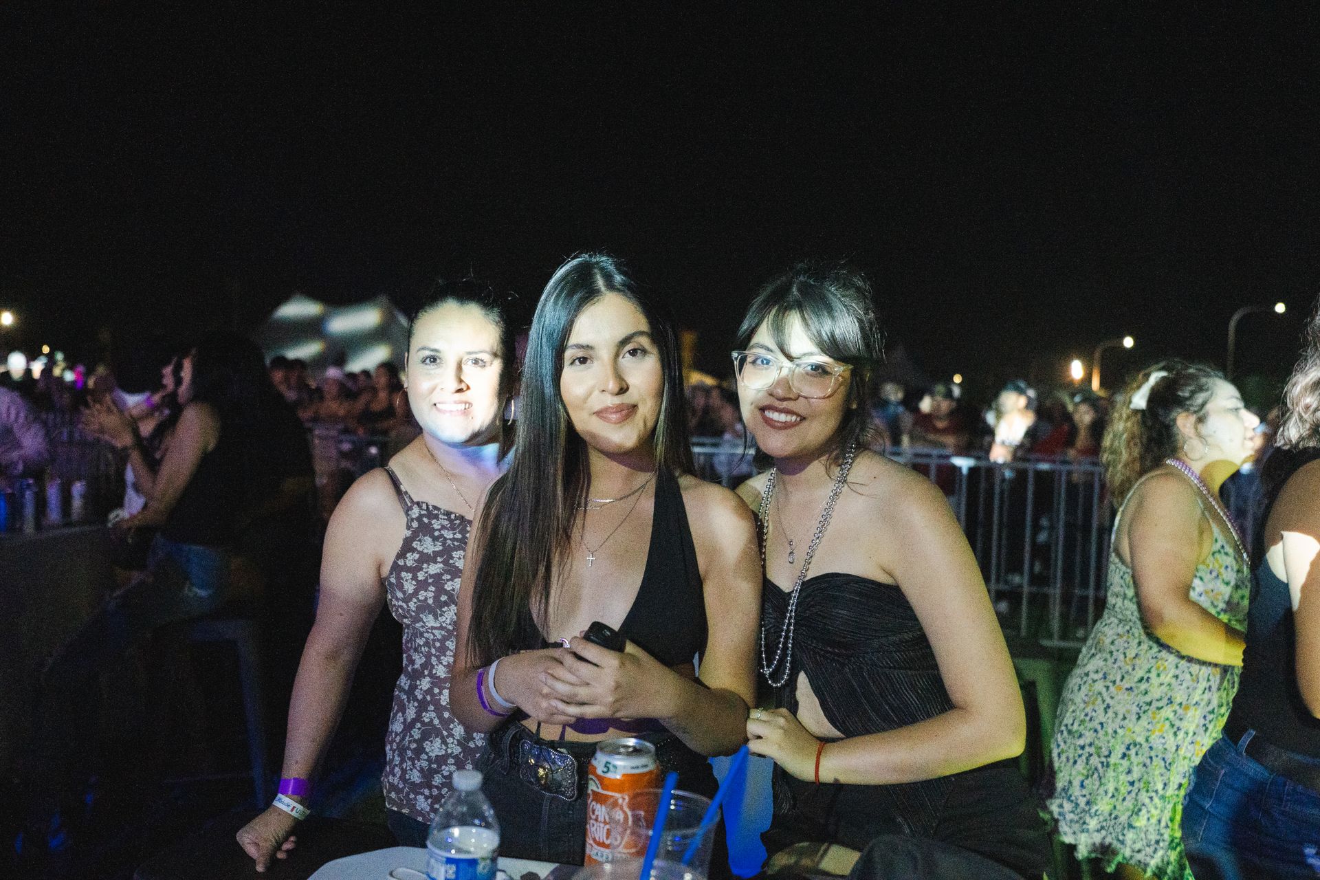 Three women are posing for a picture at a concert.