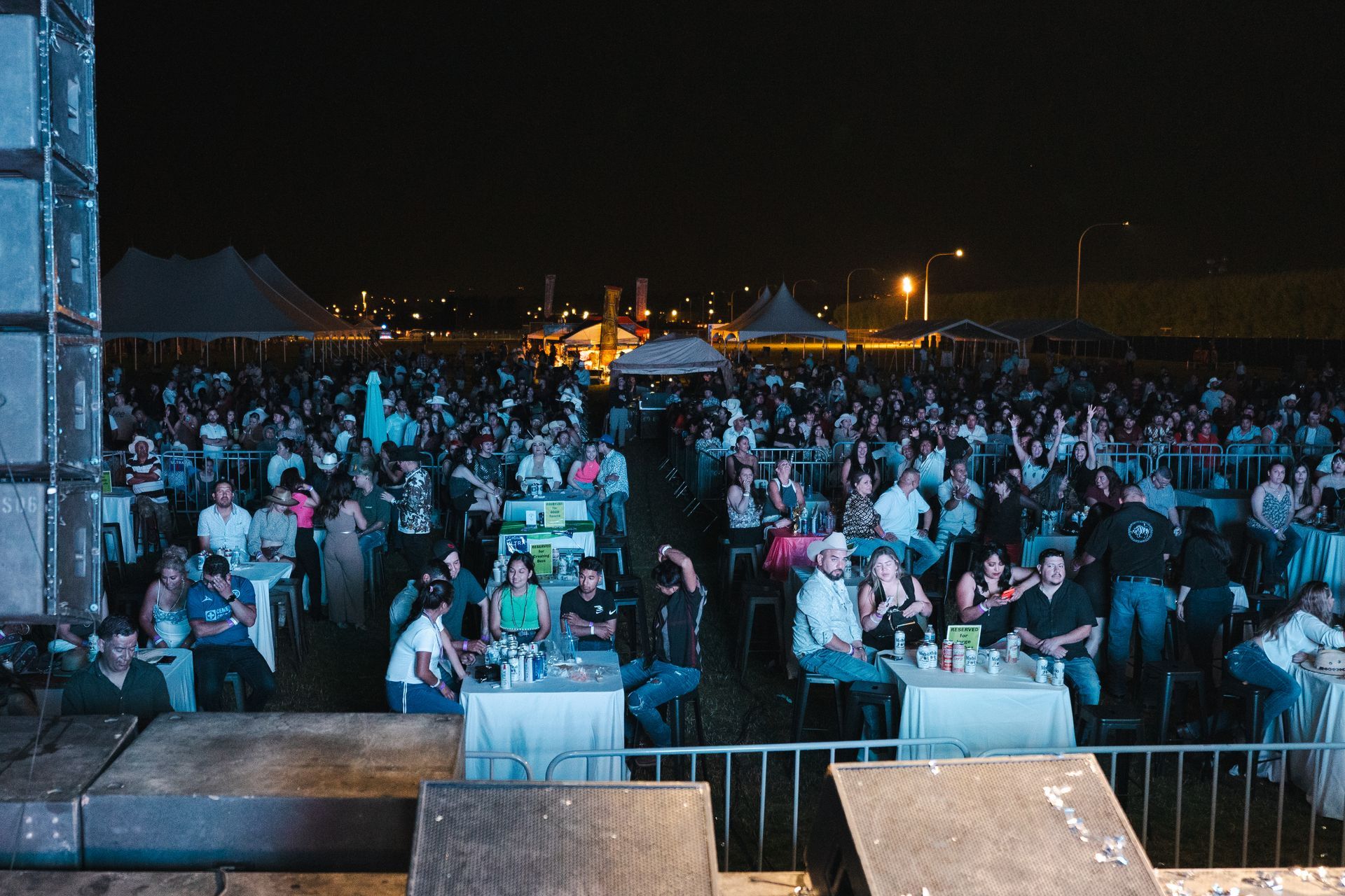 A large crowd of people are sitting at tables at a concert at night.