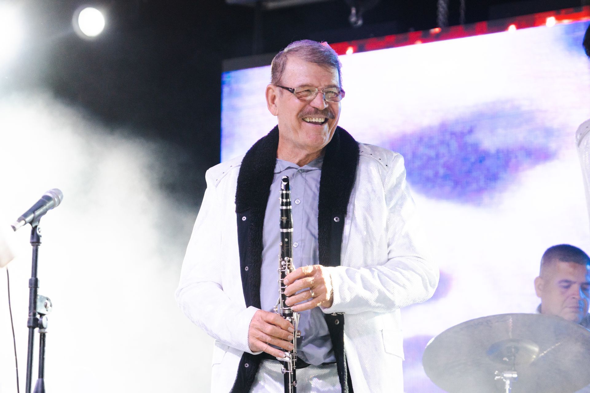 A man in a white jacket is playing a clarinet on a stage.