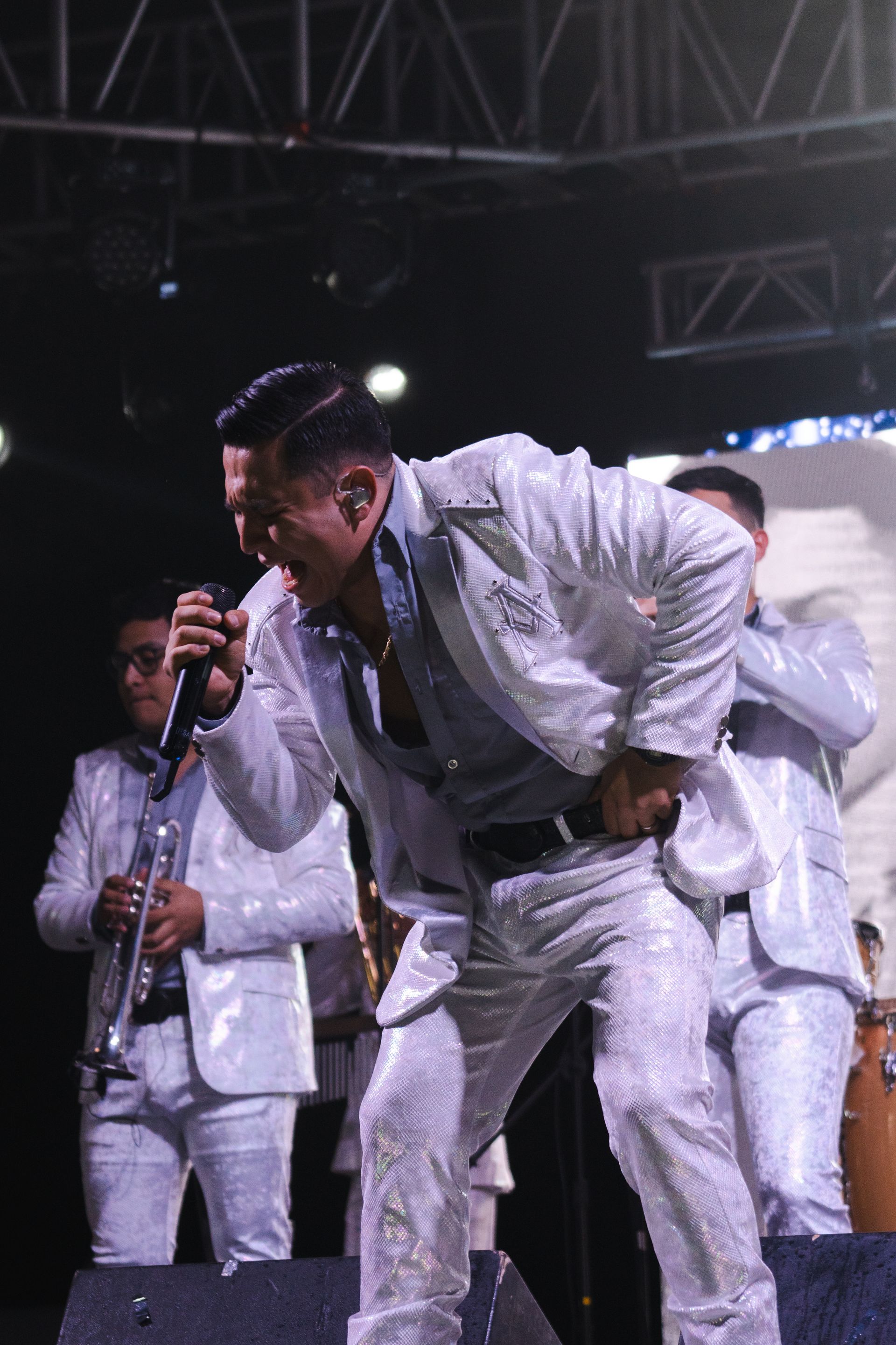 A man in a white suit is singing into a microphone on stage.