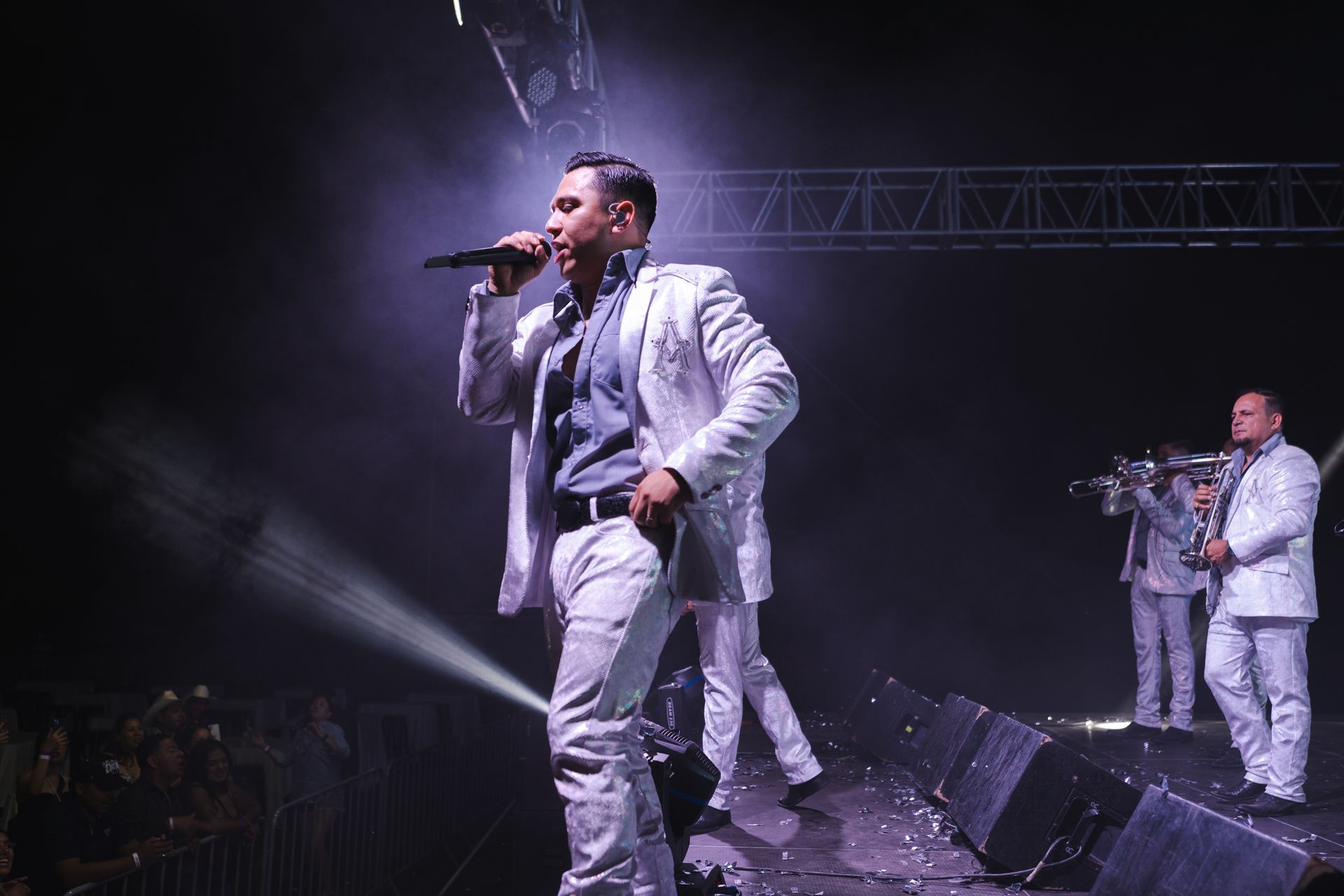 A man in a white suit is singing into a microphone on stage