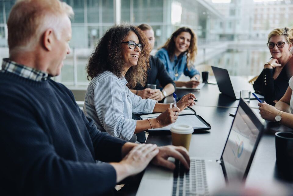 People collaborating around a conference table with laptops in a bright meeting room