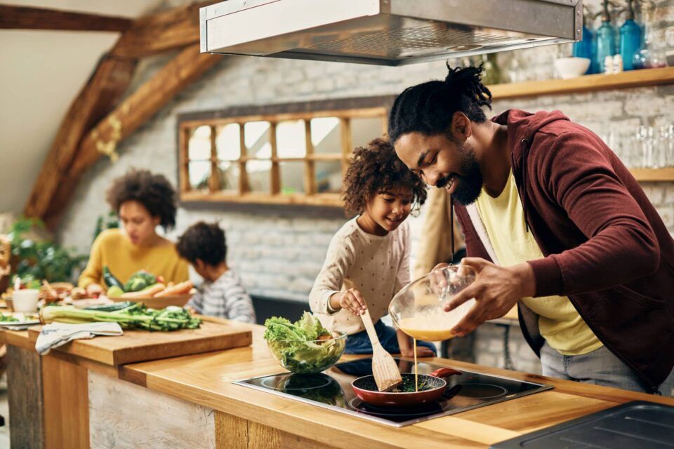 People cooking together in a bright kitchen, preparing a meal at a wooden counter.