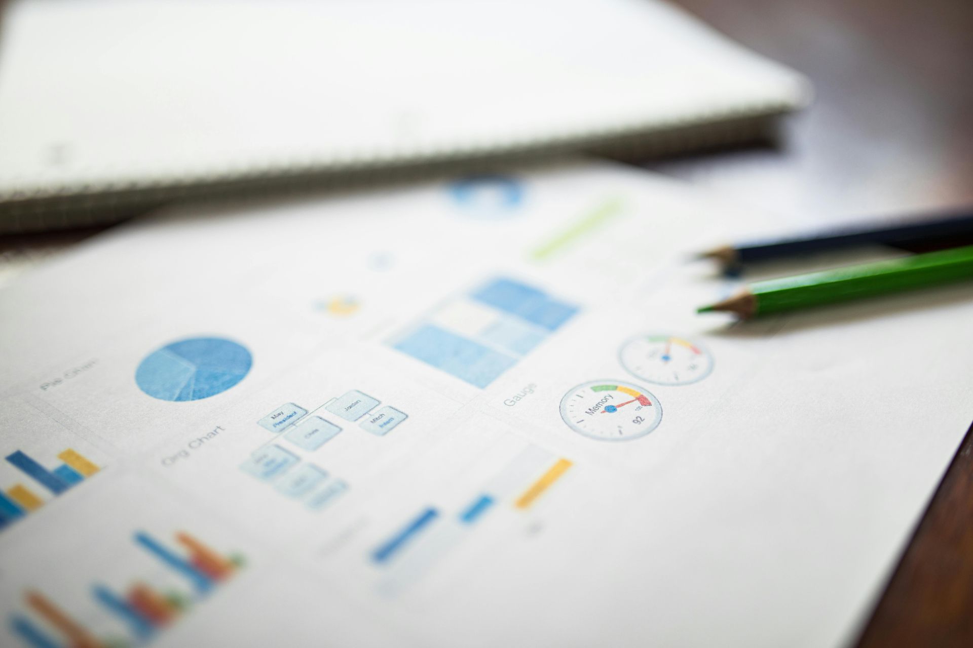 Charts and graphs on a white desk with a green pencil in the foreground
