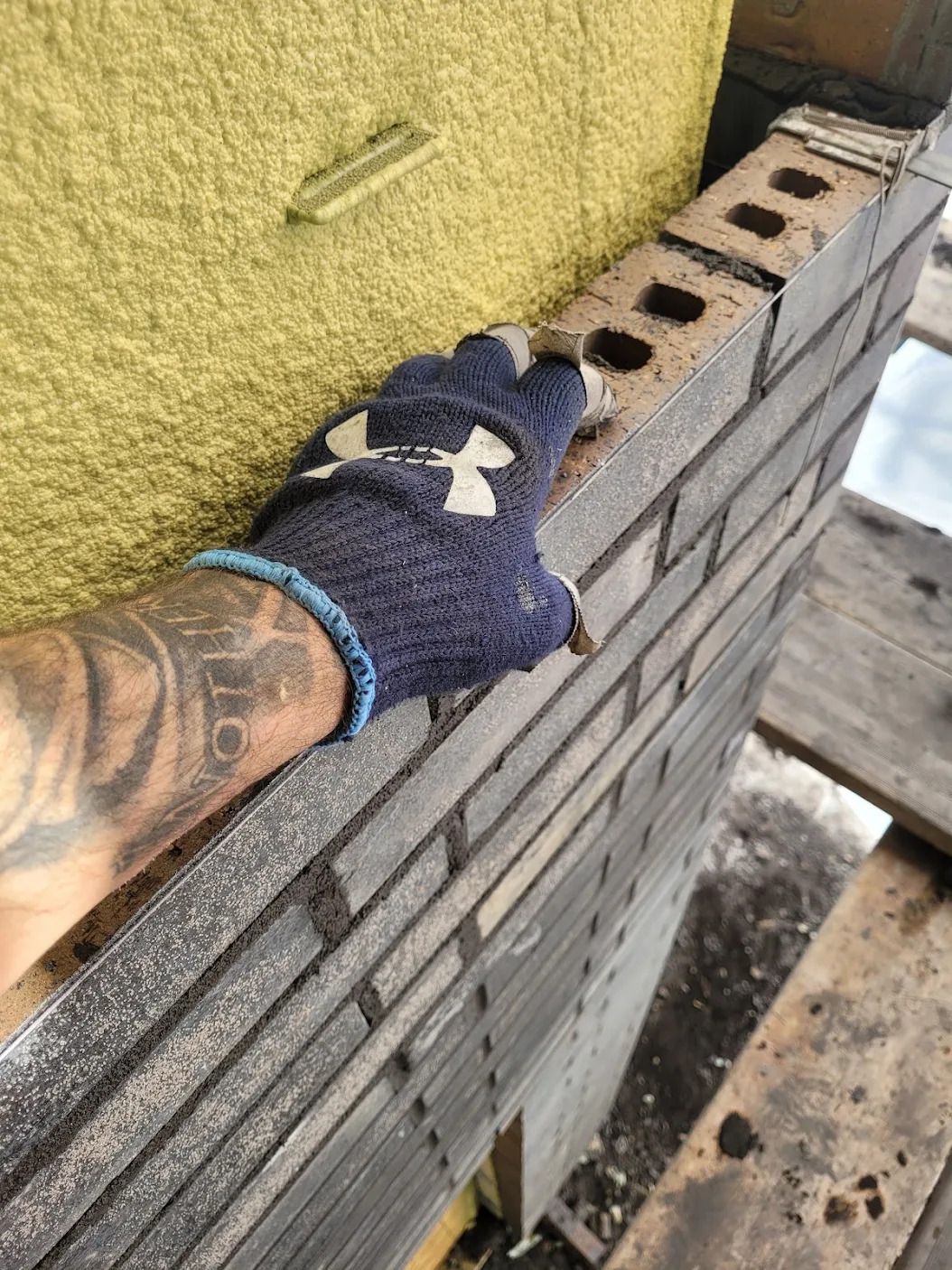 Une personne portant un gant bleu Under Armour travaille sur un mur de briques.