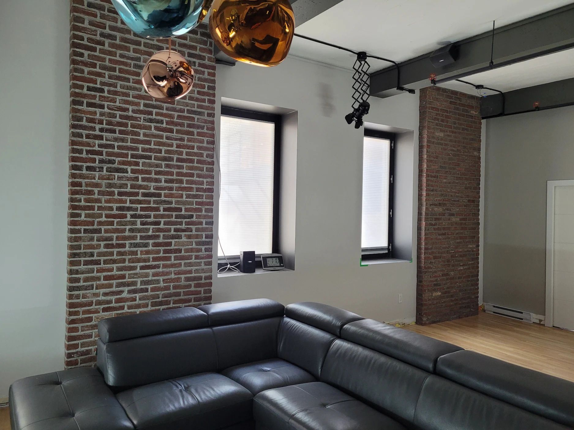 Un salon avec un canapé, deux fenêtres et un mur de briques.