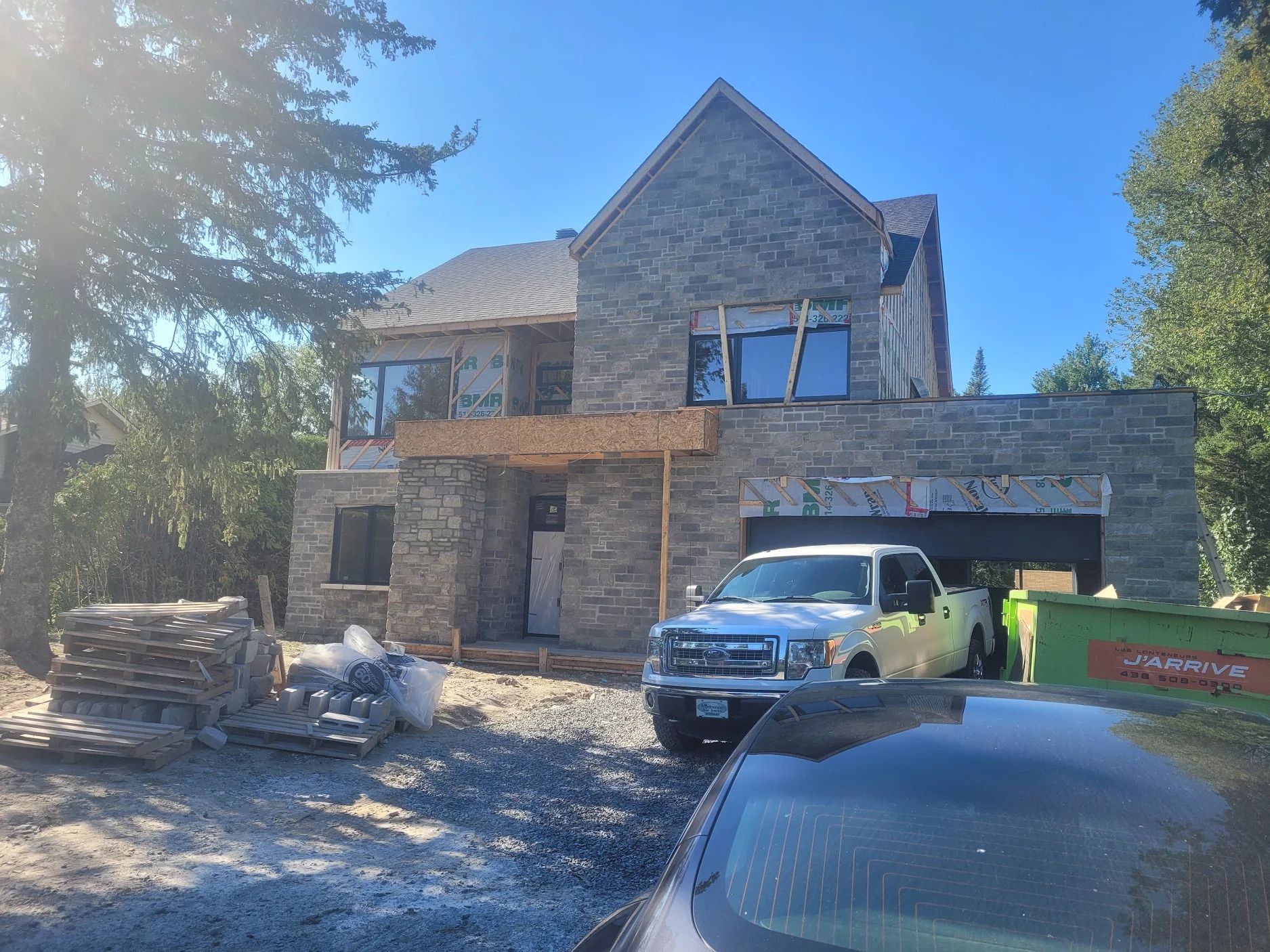 Un camion blanc est garé devant une grande maison en pierre en construction.