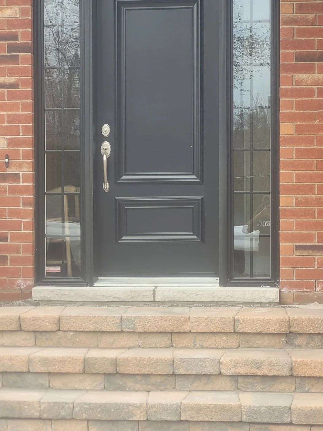 Une porte noire se trouve sur un bâtiment en briques avec des escaliers qui y mènent.