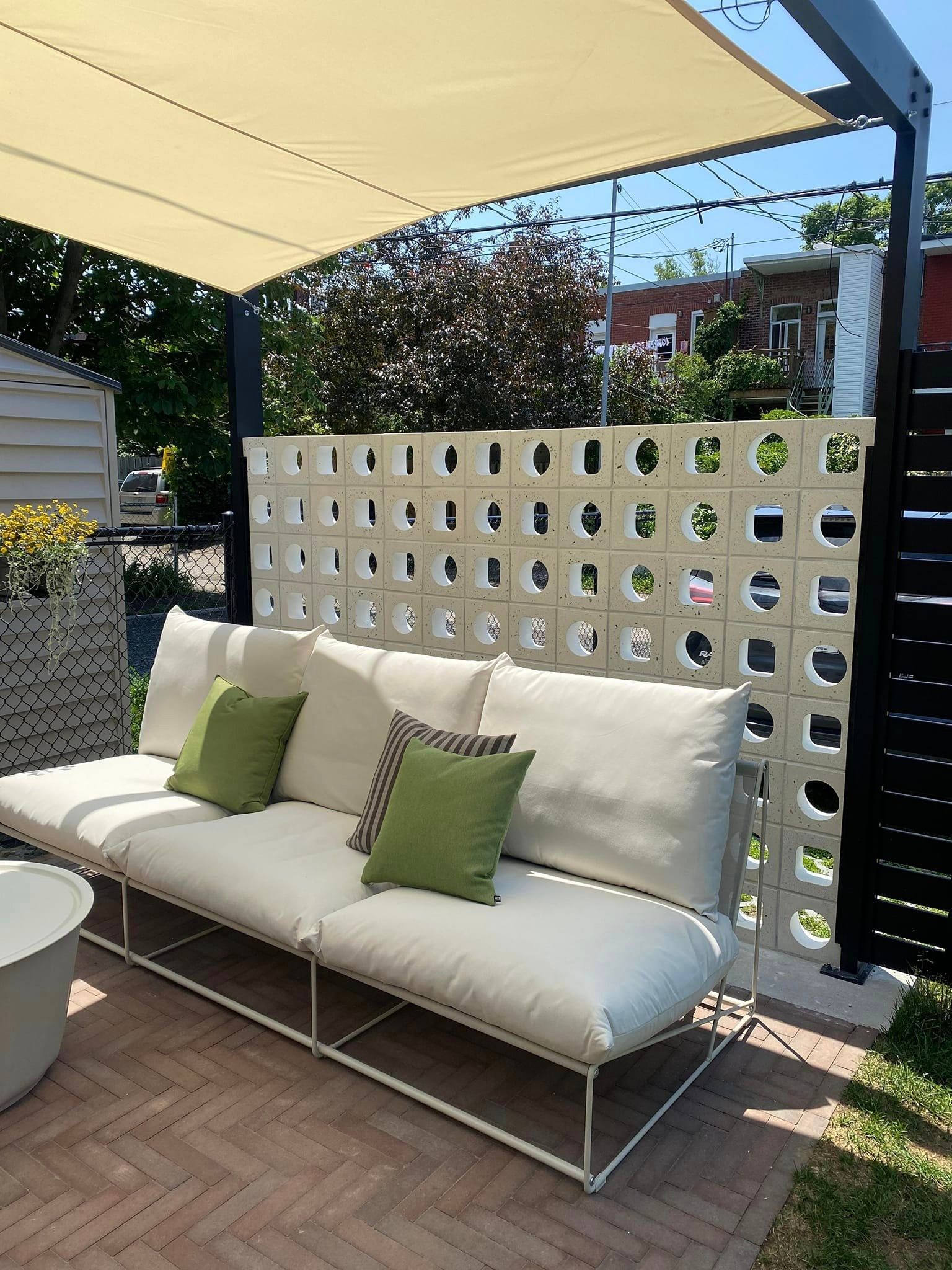 Un canapé blanc avec des coussins verts est assis sous un auvent sur une terrasse.