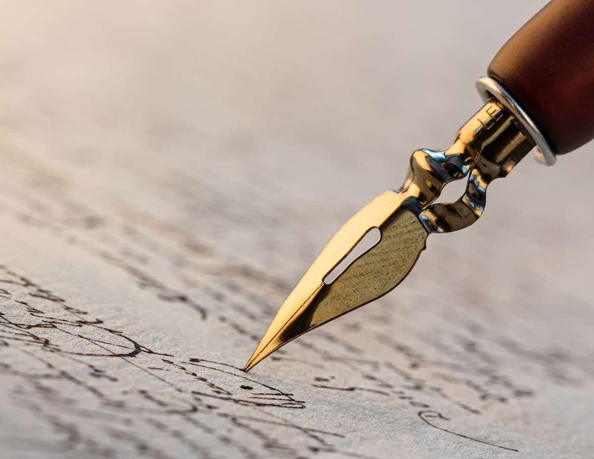 Close-up of a gold dip pen writing on parchment.