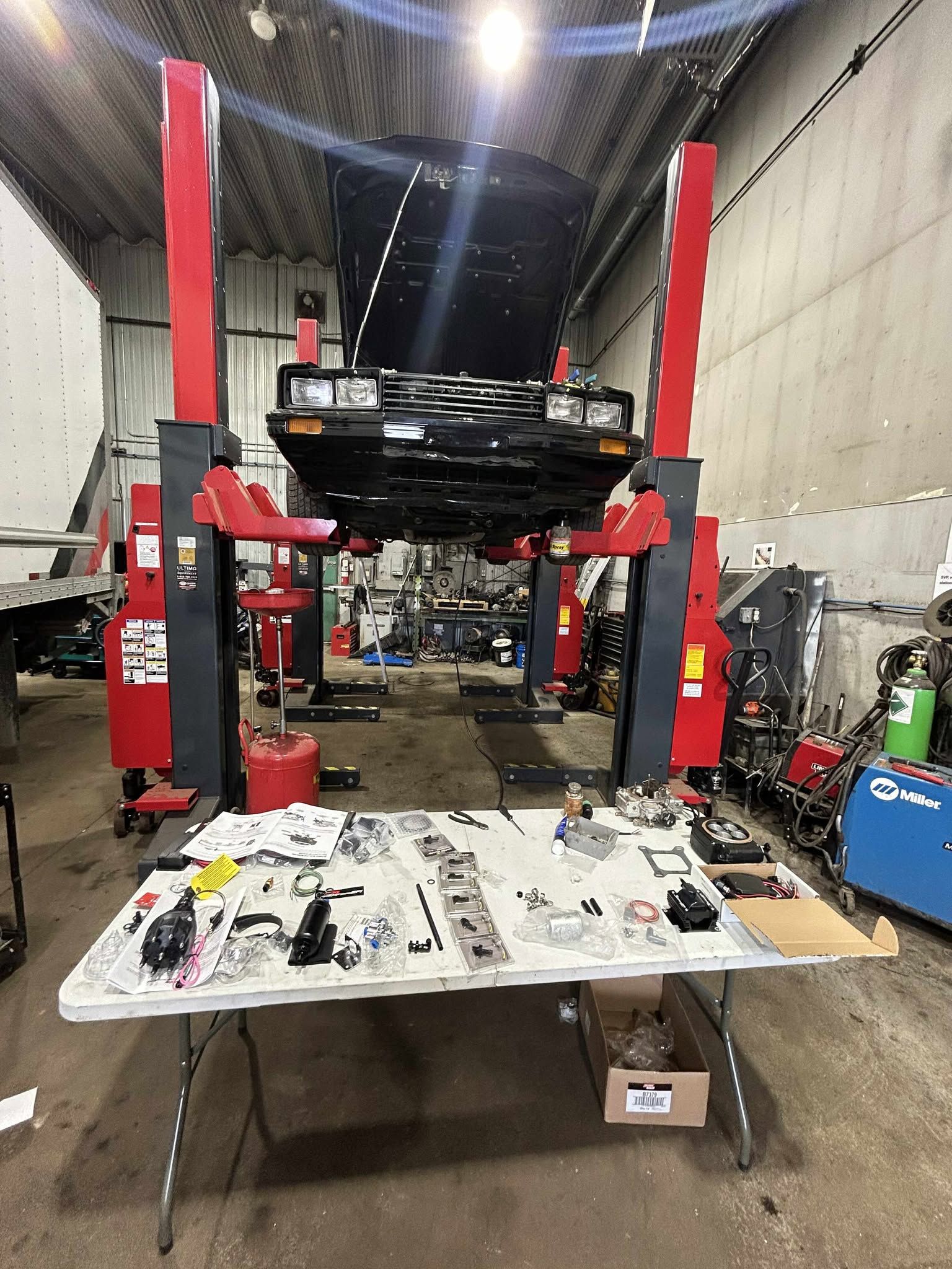 Voiture sur un pont élévateur dans un atelier, pièces détachées disposées sur une table.