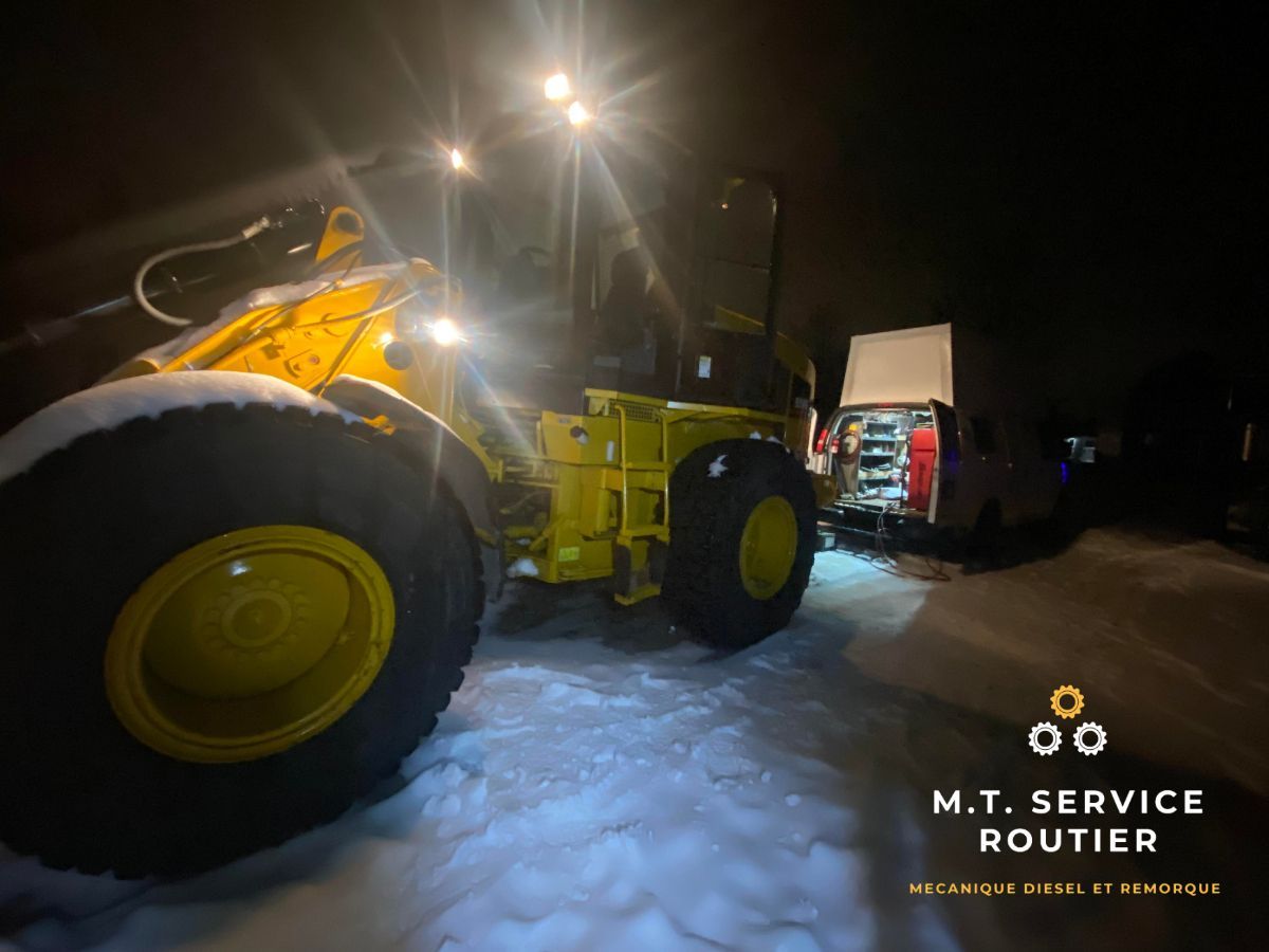 A yellow tractor is parked in the snow at night.