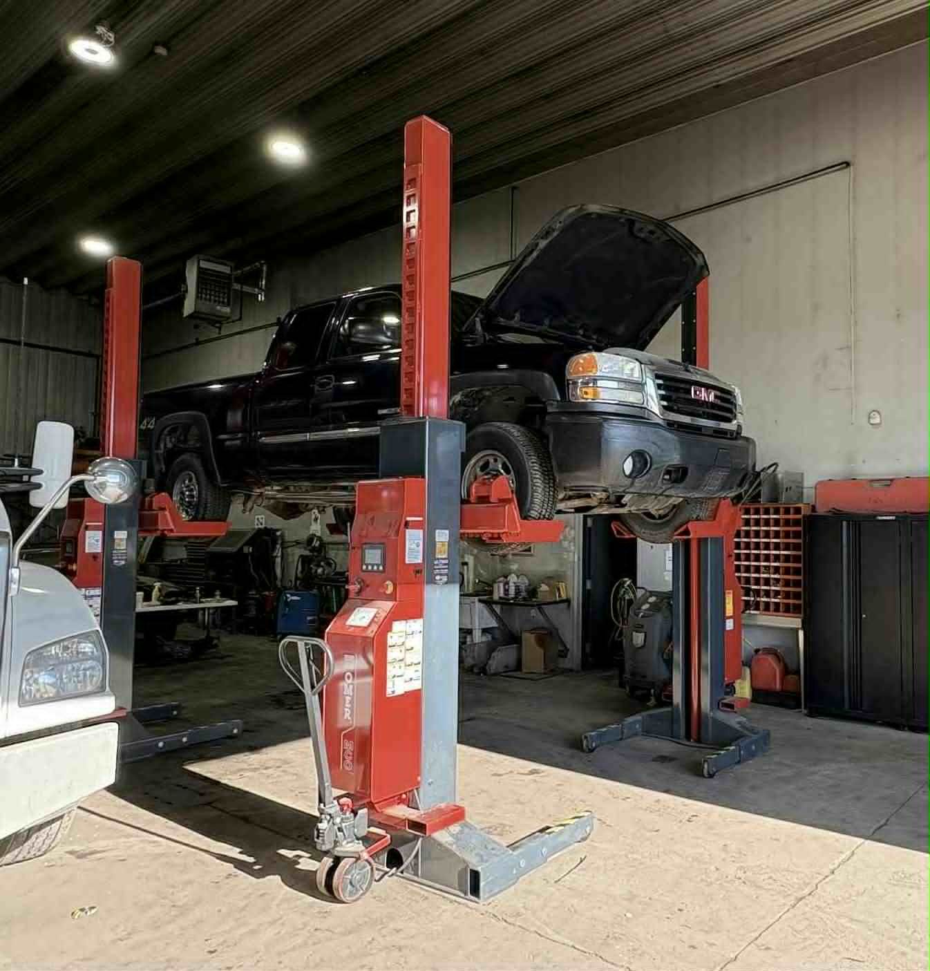 Camionnette noire soulevée sur un pont élévateur rouge à l'intérieur d'un garage ; capot ouvert.