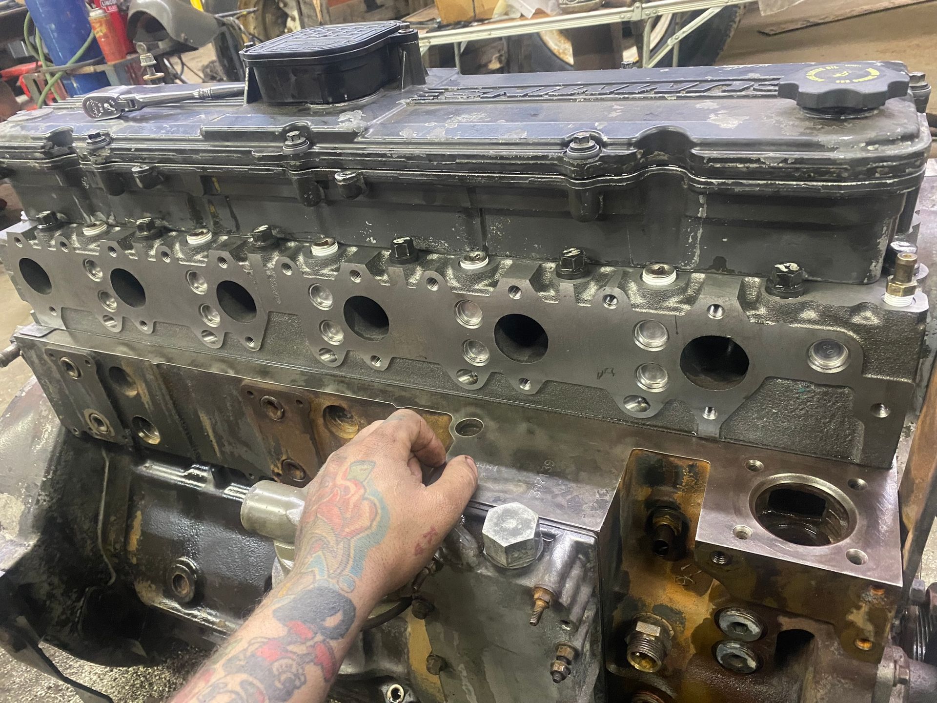 La main d'un mécanicien repose sur un moteur partiellement démonté, montrant les cylindres, la culasse et le couvre-culasse.