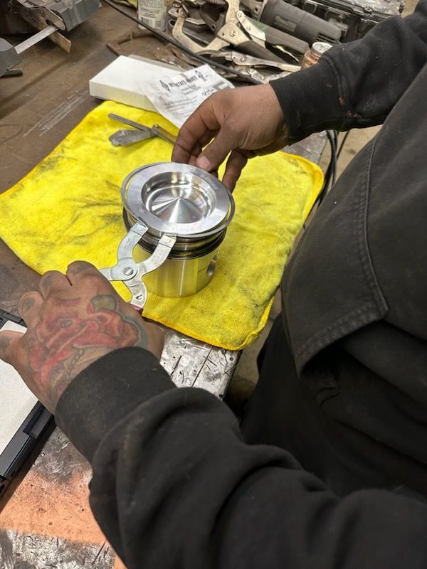 Homme utilisant un compresseur à segments de piston sur un piston dans un atelier, reposant sur un tissu jaune.