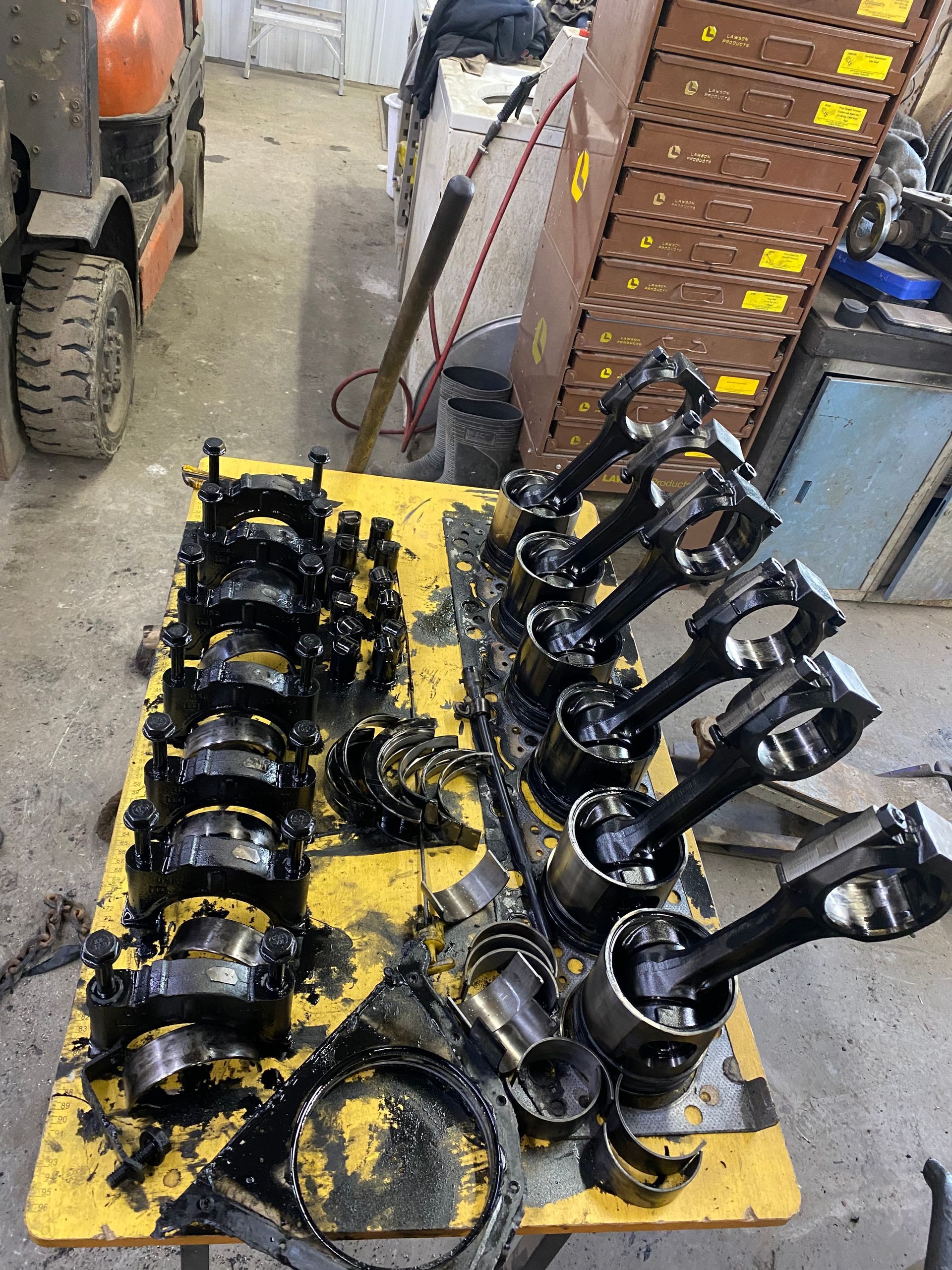 A bunch of pistons are sitting on a table in a garage.