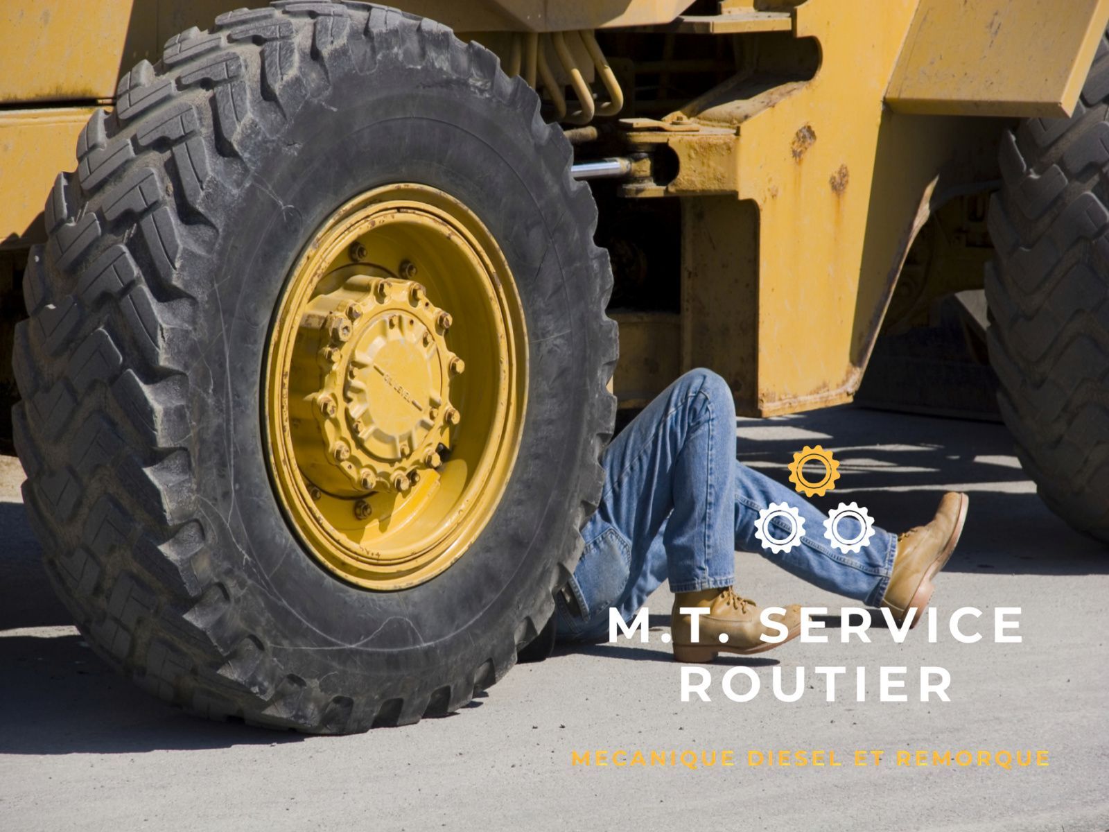 A man is laying on the ground underneath a large tire
