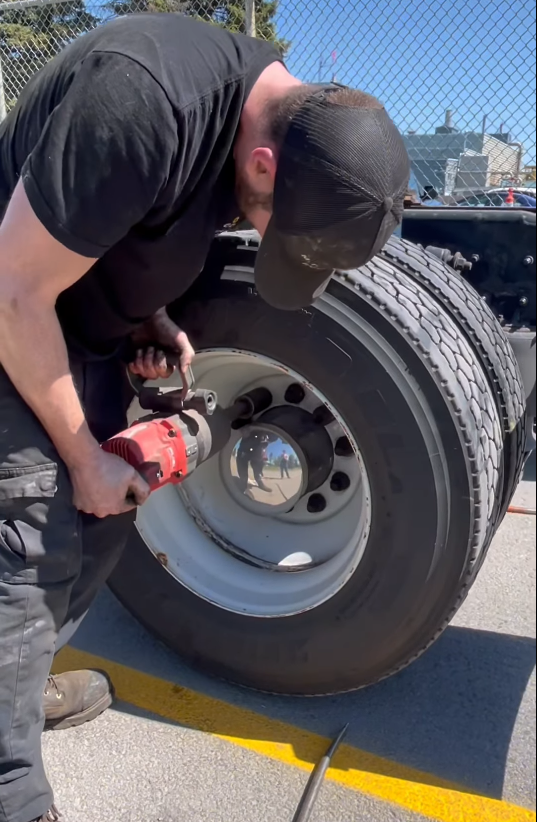 Un mécanicien utilise un outil électrique pour retirer un écrou de roue d'un pneu de camion à l'extérieur.
