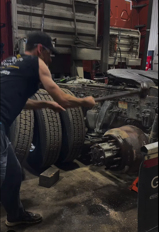 Un homme balance une masse sur l'essieu d'un camion dans un atelier de réparation.
