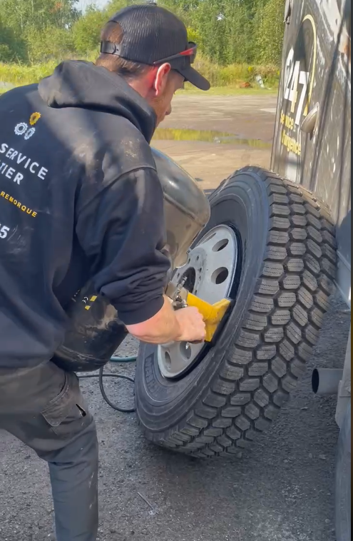 Man in black hoodie using a power tool on a truck tire outdoors.