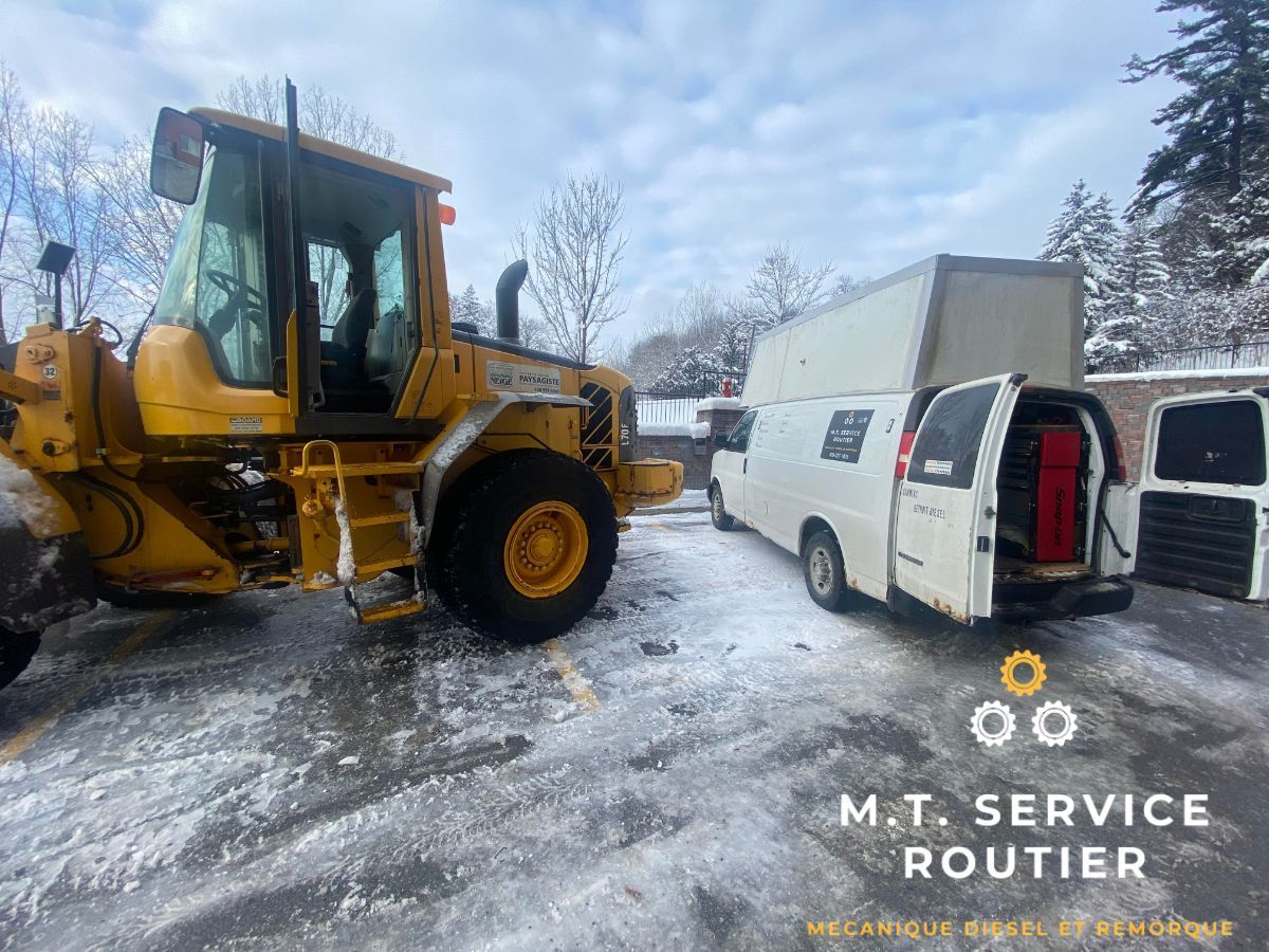 A yellow tractor is parked next to a white van in the snow.