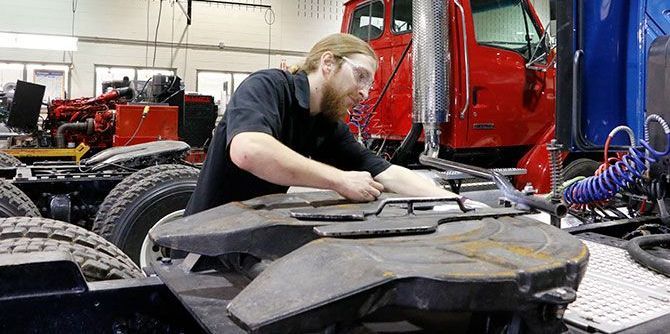 Un mécanicien portant des lunettes de sécurité travaille sur la sellette d'attelage d'un semi-remorque.