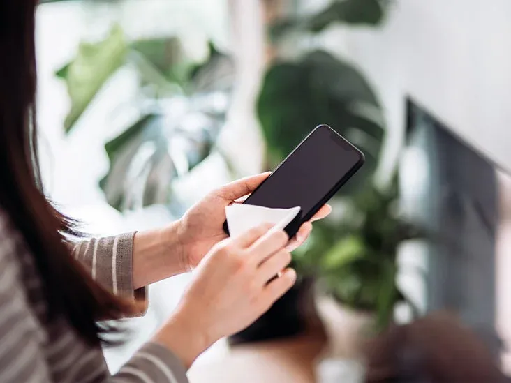 A woman is cleaning her cell phone with a cloth.