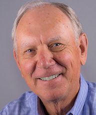 An older man in a blue shirt is smiling for the camera.