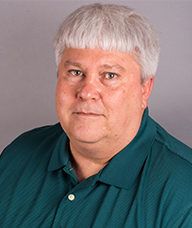 A man with white hair is wearing a green shirt and looking at the camera.
