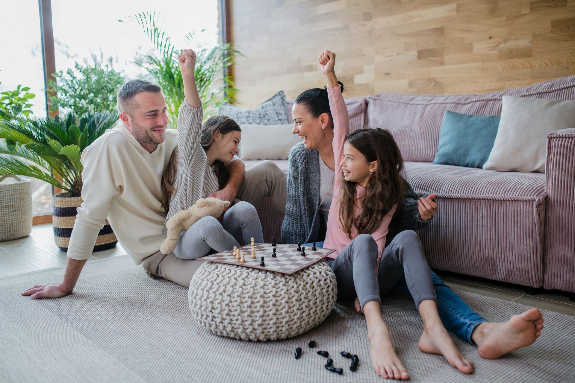 A family is sitting on the floor playing a game of chess.